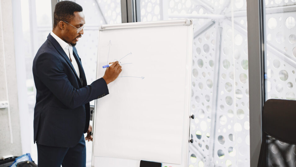 African man in a black suit. Writing board. Guy do presentation.